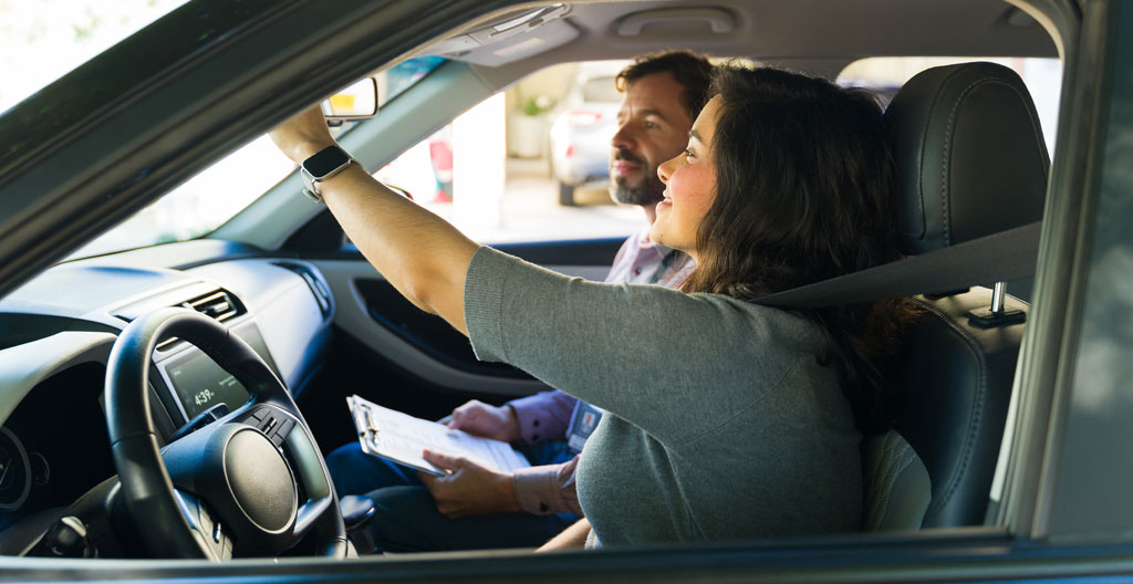 Adolescent réglant le rétroviseur intérieur d'une voiture avant de démarrer Adolescent réglant le rétroviseur intérieur d'une voiture avant de démarrer